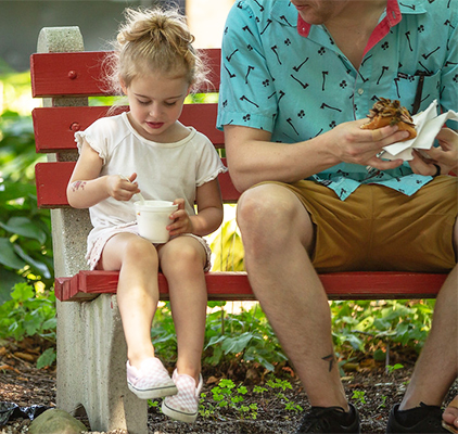 A girl on a bench with her father eating ice cream